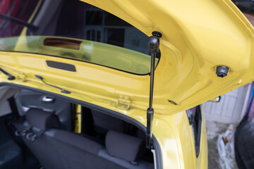 selective focus on the black bar hydraulic hinge supports on the trunk door. soft focus - obrazy, fototapety, plakaty