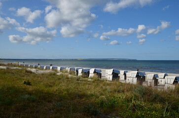 Beach chairs in the sand scenery, reed in front, sea behind, blue sky with clouds background