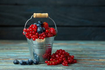 Full bucket of ripe berries - strawberries, blueberries and red currants on a wooden background