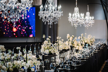 Luxury wedding reception. Table setting, setup. Banquet decoration composition flowers, candles in hall restaurant. Table covered black tablecloth. Trendy decor large chandelier for a birthday party.
