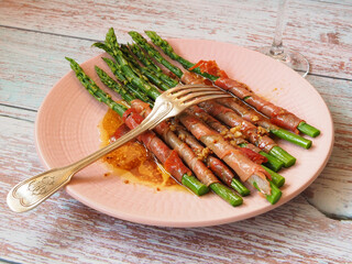 Baked or roasted asparagus with bacon or jamon and fork on a wooden background