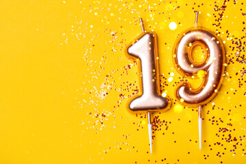 Gold candles in the form of number nineteen on yellow background with confetti. 19 years...