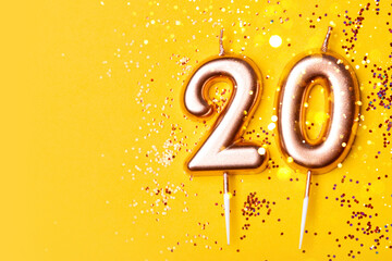 Gold candles in the form of number twenty on yellow background with confetti. 20 years anniversary...