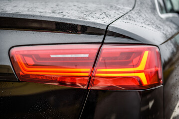 Plakat Car tail light. Detail black metallic car with rear light close up. Rear lamp signals for turning car on street. Right back modern headlight car. Signal function to keep them distance. Trunk closeup.