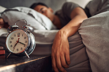 Alarm clock, relax and man sleeping in the bed of his modern apartment in the morning. Lazy, resting and closeup of a timer bell with a male person taking a nap and dreaming in bedroom at his home. - Powered by Adobe