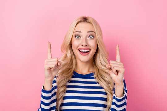Portrait of impressed overjoyed girl curly hairstyle striped pullover indicating up empty space offer isolated on pink color background