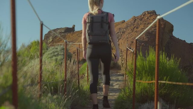 Blond woman with camera backpack walking on mountain trail in Madeira