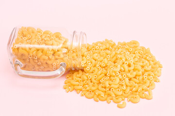 Uncooked Chifferi Rigati Pasta in Glass Jar on Pink Background. Fat and Unhealthy Food. Scattered Classic Dry Macaroni. Italian Culture and Cuisine. Raw Pasta