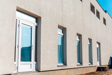 A large grey industrial business plastered wall exterior door and windows on a commercial building.Sunny summer day.