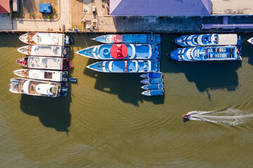 Fototapeta na wymiar Aerial view of tour boats moored at marina with dinghy speeding nearby. Top view from drone of motorboats in dock at phuket, Thailand. Nautical vessel transportation business and marine tourism