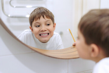 cute 8 years old boy washing face in bathroom looking in mirror and smiling.