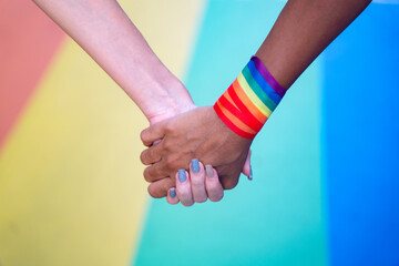 Close-up lesbian couple holding hands with rainbow background. LGBTI concept.