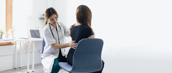 Doctor is diagnosing female patient with back pain in examination room at hospital.