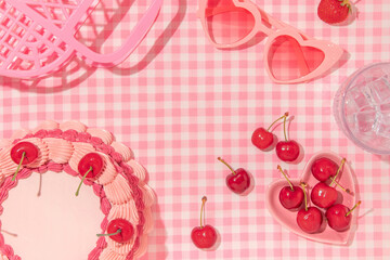 Summer creative layout with vintage cake, cherries, glass with ice cubes, heart sunglasses and handbag on pastel pink plaid background. 80s or 90s retro aesthetic idea. Minimal summer fruit idea.