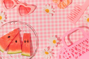 Summer creative layout with watermelon, slices, heart sunglasses, flowers, hair comb, scrunchy and handbag on pastel pink plaid background. 80s or 90s retro aesthetic idea. Minimal summer idea.