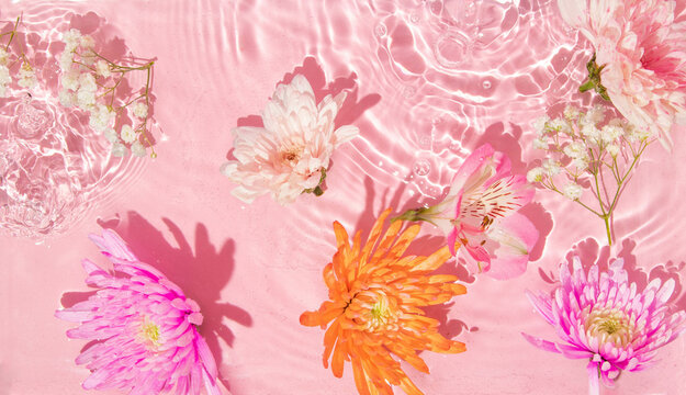 Summer creative layout with pink, orange flowers in pastel pink water ripple background. 80s or 90s retro aesthetic fashion cosmetic idea. Minimal summer idea.