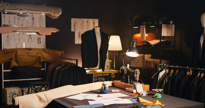 Fashion atelier with clothes sketches and tools, sewing machines and instruments used to create tailored items at workstation. Empty tailoring space with drawings and materials. Handheld shot.