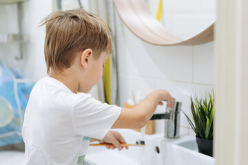cute 5 years old boy brushing teeth with bamboo tooth brush in bathroom rinsing brush with water