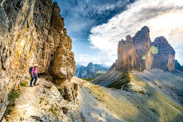 Young athletic woman enjoys scenic view on Tre Cime from via ferrata in the evening. Tre Cime, Dolomites, South Tirol, Italy, Europe.