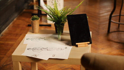 Sewing shop with clothes sketches and fashion items on papers, handmade textile industry atelier with tools. Empty workshop with drawings for tailored custom made clothing. Close up.