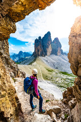 Young athletic woman enjoys scenic view on Tre Cime from via ferrata in the evening. Tre Cime,...
