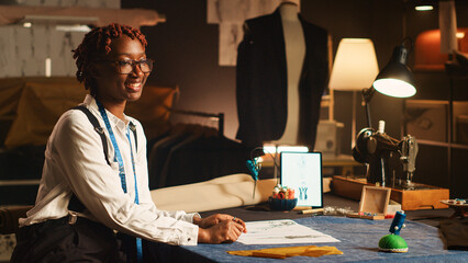 Female couturier works on clothes design, looking at sketches to create luxury clothing line at atelier workstation. Tailor employee handmade items for luxury workshop collection.