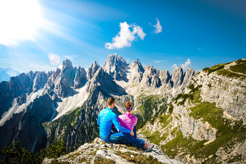 Naklejka premium Sitting young couple enjoys epic view on Cadini di Misurina mountain range in the morning. Tre Cime, Dolomites, South Tirol, Italy, Europe.