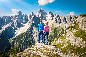 Fototapeta premium Athletic young couple enjoys epic view on Cadini di Misurina mountain range in the morning. Tre Cime, Dolomites, South Tirol, Italy, Europe.