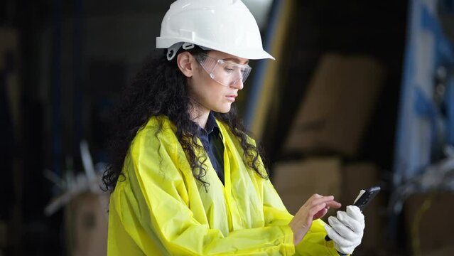 Long-haired manager in hardhat searches contact on smartphone for reporting working process at waste plant. Supervisor controls waste sorting factory