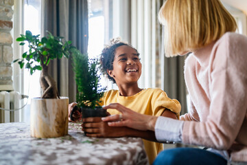 Happy caucasian mother and her adopted african american daughter taking care of plants indoors.