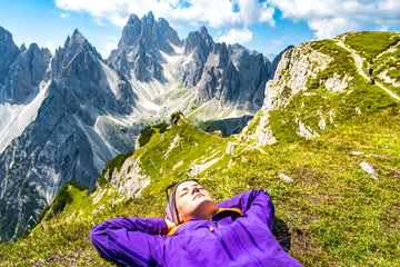 Young woman enjoys sunbath with epic view on Cadini di Misurina mountain range in the morning. Tre...