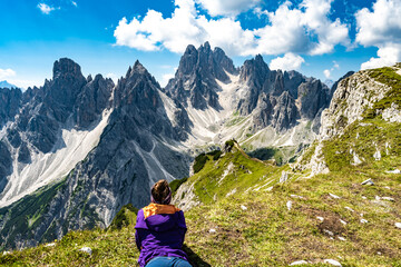 Fototapeta na wymiar Lying woman enjoys epic view on Cadini di Misurina mountain range in the morning. Tre Cime, Dolomites, South Tirol, Italy, Europe.
