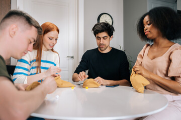 Portrait of relaxed multiethnic friends playing gambling board game sitting at table in living room with modern interior. Playful multiracial people enjoying leisure activity on weekend day at home.