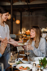 Young woman blowing candles on cake while celebrating birthday among friends in restaurant