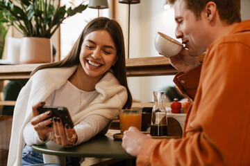 Happy couple using mobile phone while sitting in cafe