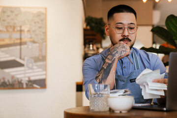 Business owner working with financial bills and calculates profit while sitting in cafe