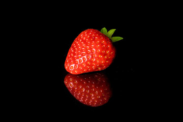 Strawberries isolated on black background. One whole fresh red strawberry close-up.