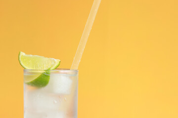 Lemonade with ice and lime on a bright orange background. Summer cocktail with cold drink. Copy space. Drink with a straw close-up