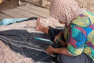 Cambogia,donna anziana aggiusta una rete da pescatore - obrazy, fototapety, plakaty