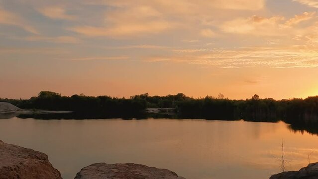 Beautiful sunset and cloudy sky over a forest lake at evening in vacation, showing the gentle lake ripples and waves at sunset, with a slow pan, revealing the reflection of the setting sun. High. High