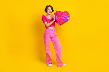 Full size photo of gorgeous impressed girl wear knit top pink pants hold large purple paper like isolated on yellow color background