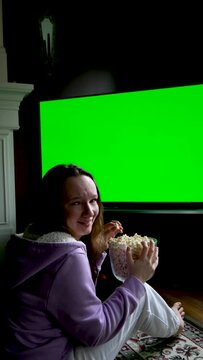 Woman Watching Green Chroma Key Screen TV Relaxing. Girl in Cozy Room Watching Sports Match, News, Sitcom TV Show or a Movie on Green Screen eating popcorn and Change TV channels