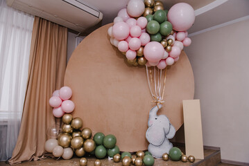 Birthday party for girl or boy on brown photo wall. Arch decorated pink, golden, green balloons, paper decor elephant, confetti. Children's photo zone. Celebration baptism concept. Space for text.