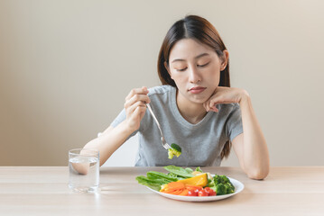 Obraz na płótnie Canvas unhappy asian women is on dieting time looking at broccoli on the fork. girl do not want to eat vegetables and dislike taste