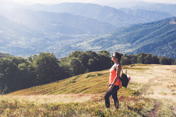 Fototapeta premium Full-length woman on top of a mountain rests and enjoys a sunny day and breathes while embracing the environment. Hiking in the mountains for women's health after 40 years