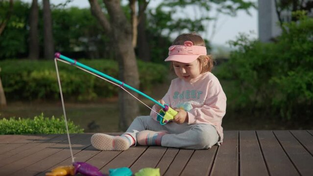 Happy Age 3 Little Girl Caught Toy Plastic Fish on Magnatic Fishing Rod While Playing Educational Game Outside Sunset Time in Spring Park. Preschooler Learning Concept