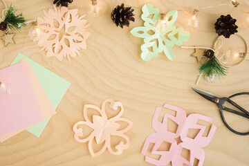 Fototapeta na wymiar Colorful paper snowflakes cutouts, on a wooden background. Cutting snowflakes from colored paper. Snowflake winter background. Simple winter kids crafts idea. Copy space