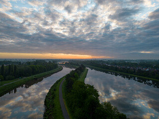 Sunrise or sunset over the river and beautiful morning or evening landscape of Duffel, Antwerp, Belgium. Evening sun breaks through the clouds and the trees. Flight over calm river with reflection