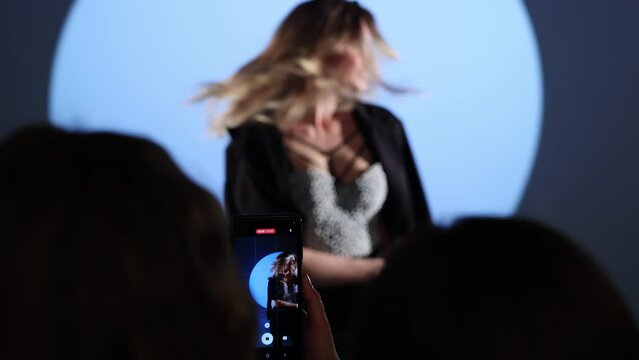 Photographer takes pictures of a female model in the studio on a mobile phone.