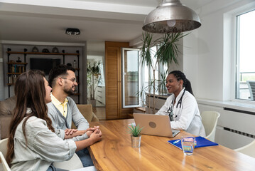 Woman doctor visits a young married couple in their home and gives health consultations. Female medical worker in a patients apartment listening about health and giving pregnancy advice